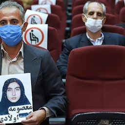 أحد أفراد عائلة ضحية يحمل صورتها أثناء المحاكمة الغيابية لأعضاء منظمة مجاهدي خلق المزعوم تورطهم في قتل مدنيين في الثمانينيات في طهران، إيران. 7 مارس/آذار 2021 (الصورة عبر وكالة ميزان للأنباء)