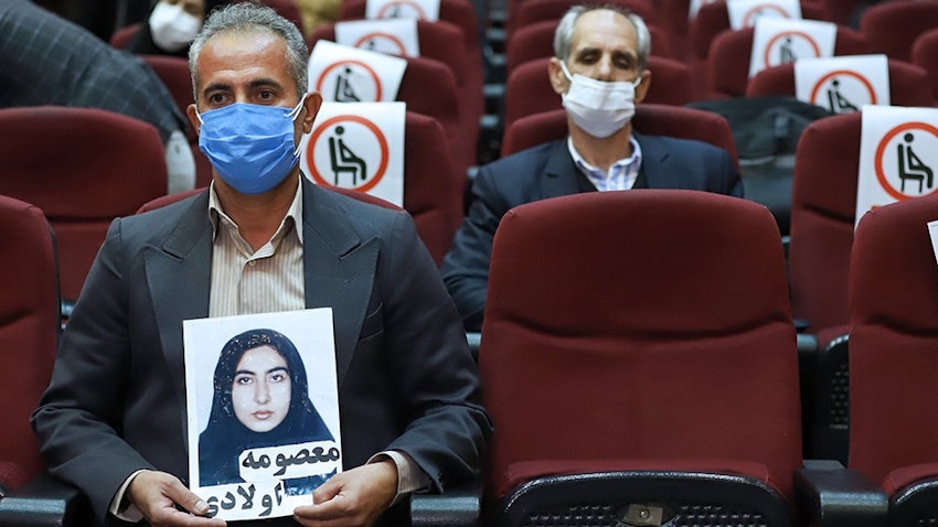 أحد أفراد عائلة ضحية يحمل صورتها أثناء المحاكمة الغيابية لأعضاء منظمة مجاهدي خلق المزعوم تورطهم في قتل مدنيين في الثمانينيات في طهران، إيران. 7 مارس/آذار 2021 (الصورة عبر وكالة ميزان للأنباء)