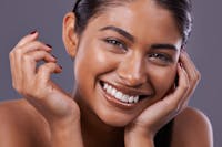 Gorgeous woman smiling in her 20's is having her portrait taken. Her hair is tied back. Her skin is glowing as she looks directly at the camera. Her glowing skin is to emulate the potential results of using the Acorn Treatment
