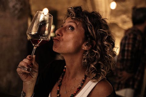 Claudia Piras guarda un calice di vino in un ambiente raccolto e illuminato da luci calde.