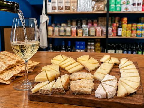 A glass of Vermentino being poured beside a board with assorted cheeses and pane carasau