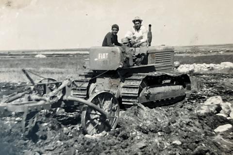 Fotografia storica in bianco e nero di due uomini su un trattore agricolo durante i lavori nei campi.