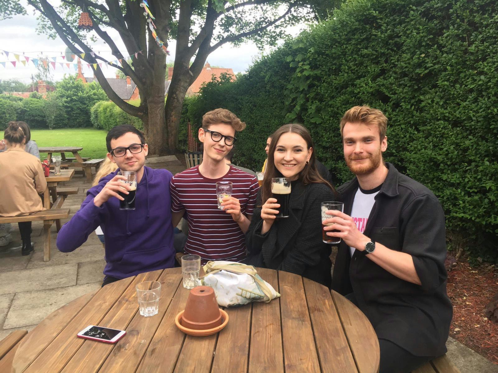 Alex and three friends sit at a round pub table outdoors