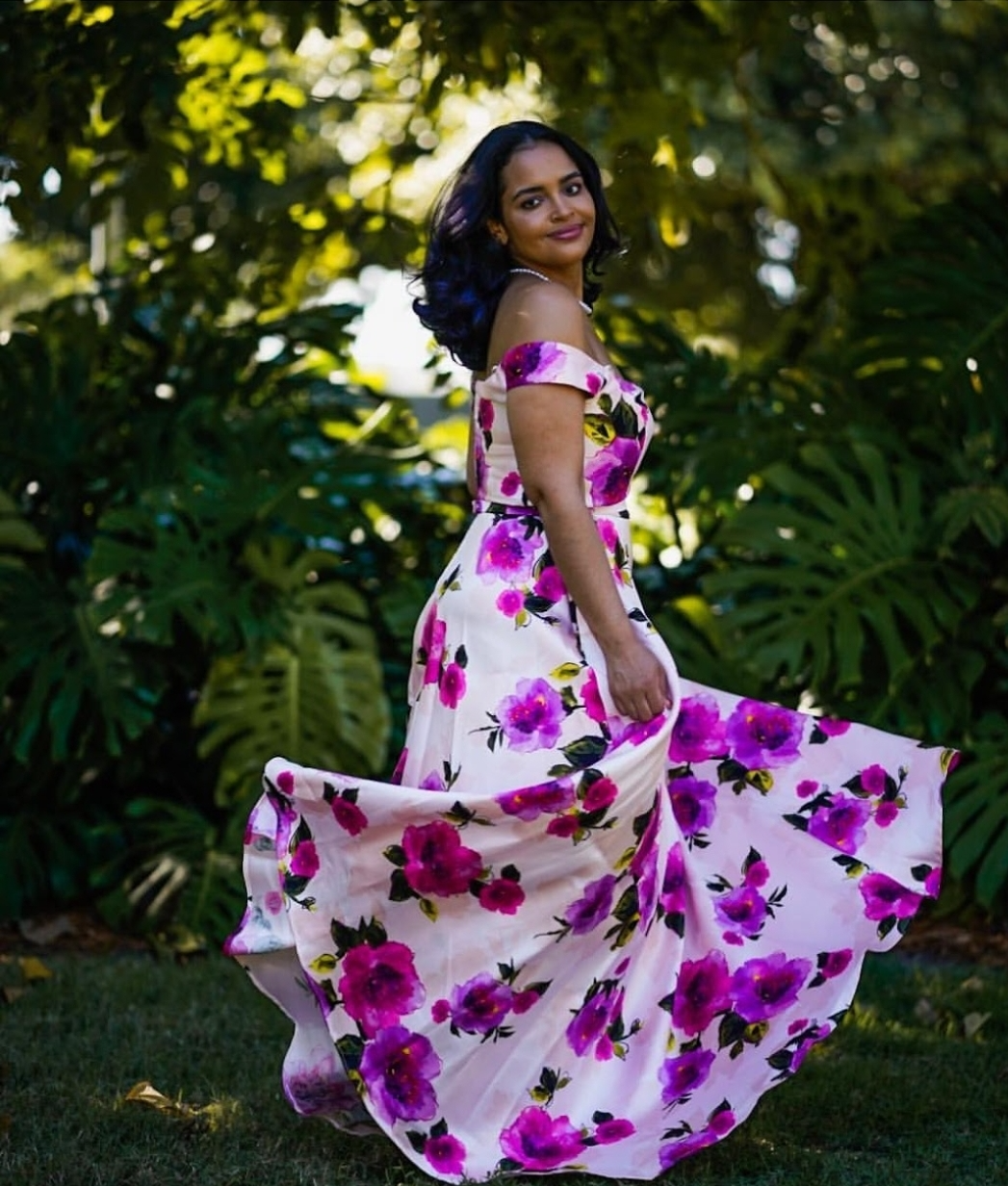 Full length picture of a young woman with long dark hair and a purple flowery dress which she is swirling.