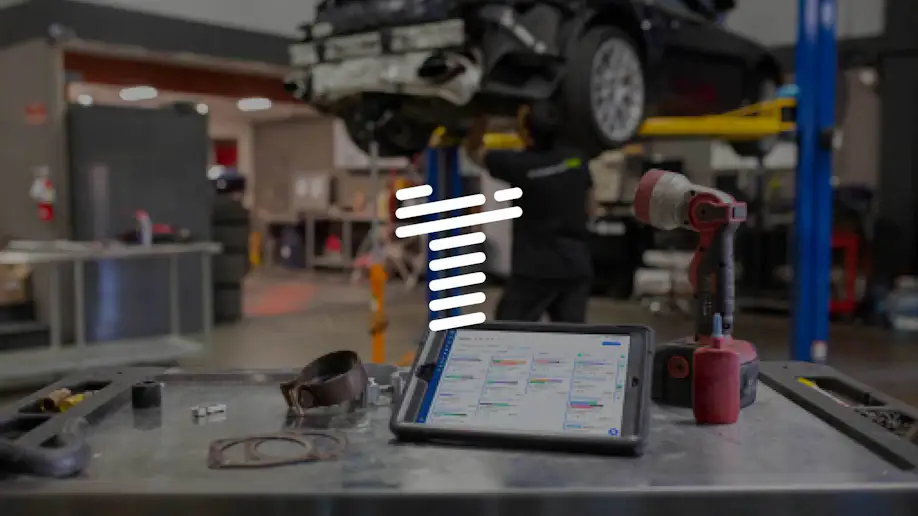 A stylized T over a background of an auto shop with an iPad using Shopmonkey.