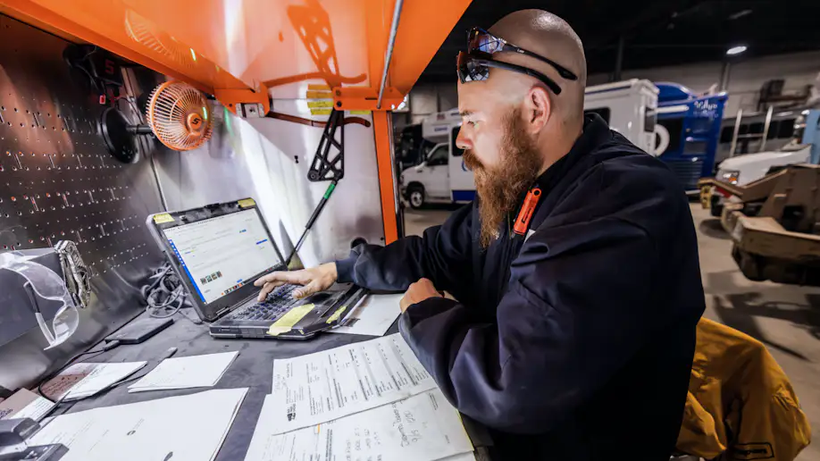 A man with a red beard, wearing 2 sets of sunglasses doing paperwork in an auto shop.