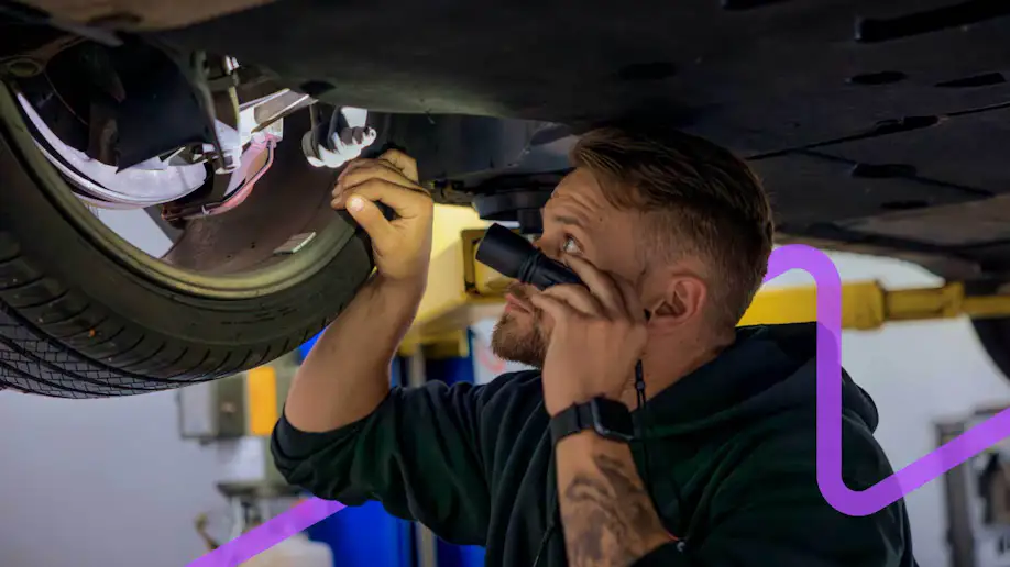 A man with a flashlight inspecting the undercarriage of of a car.