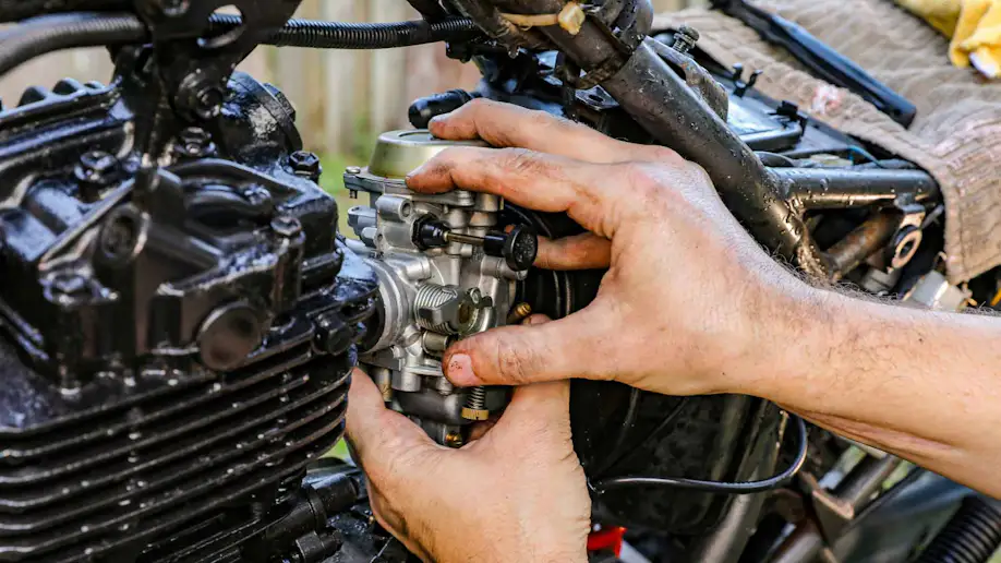 An auto technician cleaning a motorcycle carburetor.