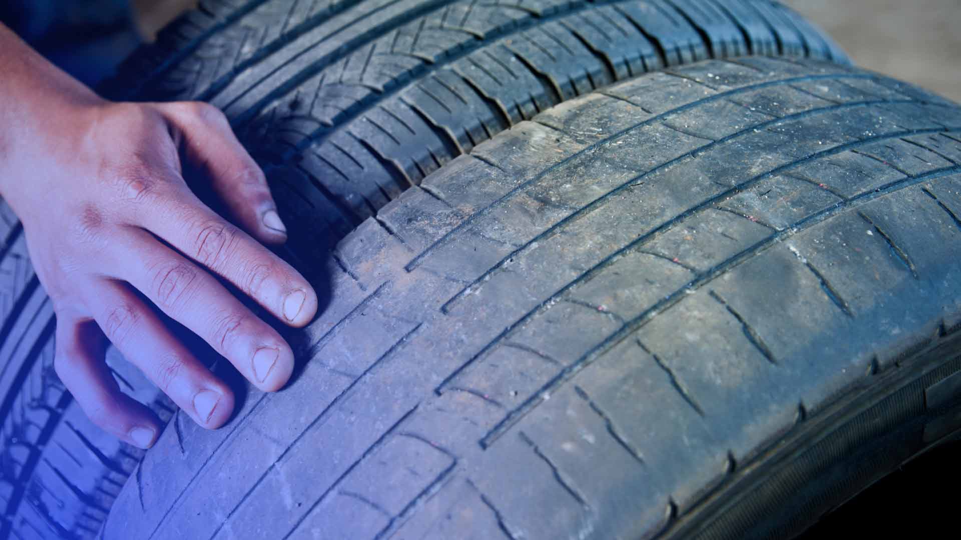 A tire shop technician inspecting two tires.
