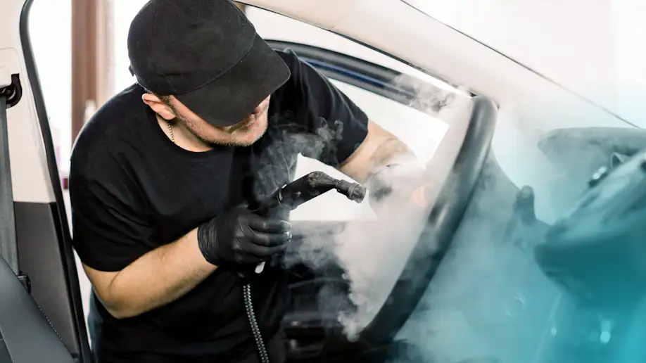 An auto detailer steam washing the interior of a vehicle.