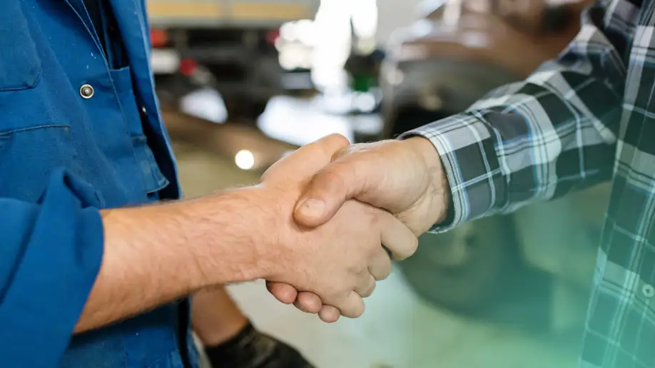 An auto shop owner and a mechanic shaking hands.