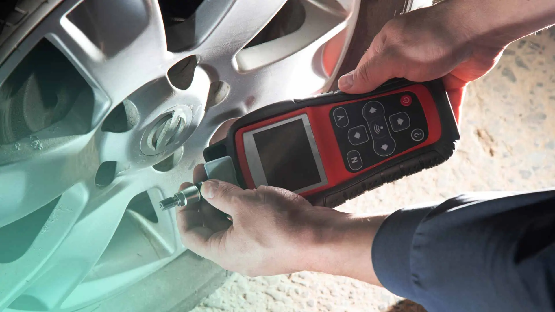An auto mechanic using a tire pressure monitoring tool.
