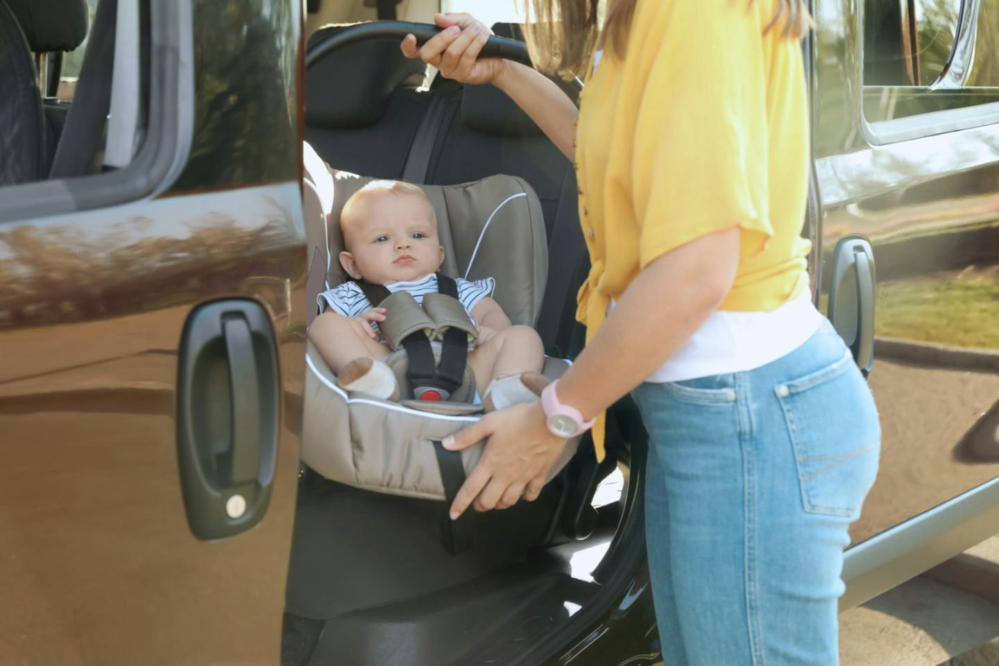 Mum lifting her baby in a car seat out of the car