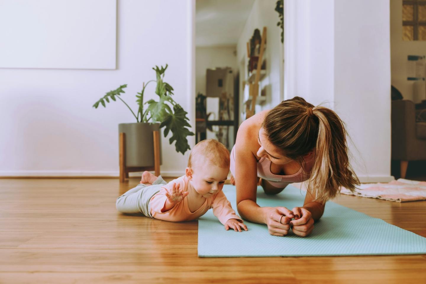 Mum doing a forearm plank on a yoga mat beside her baby