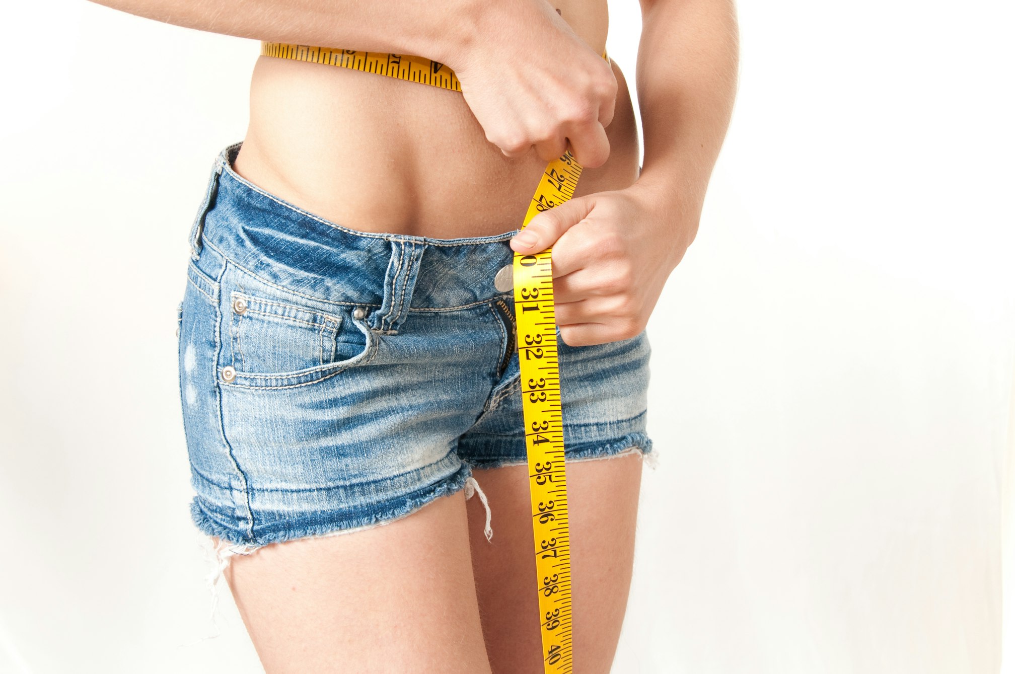 Woman measuring waist wearing denim shorts