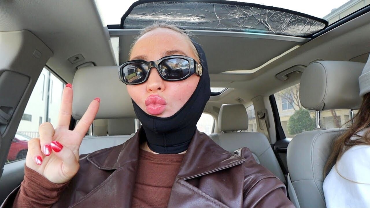 Photo of Chin AirSculpt + recipient Kenzie Elizabeth in her car with a compression garment on giving the peace sign