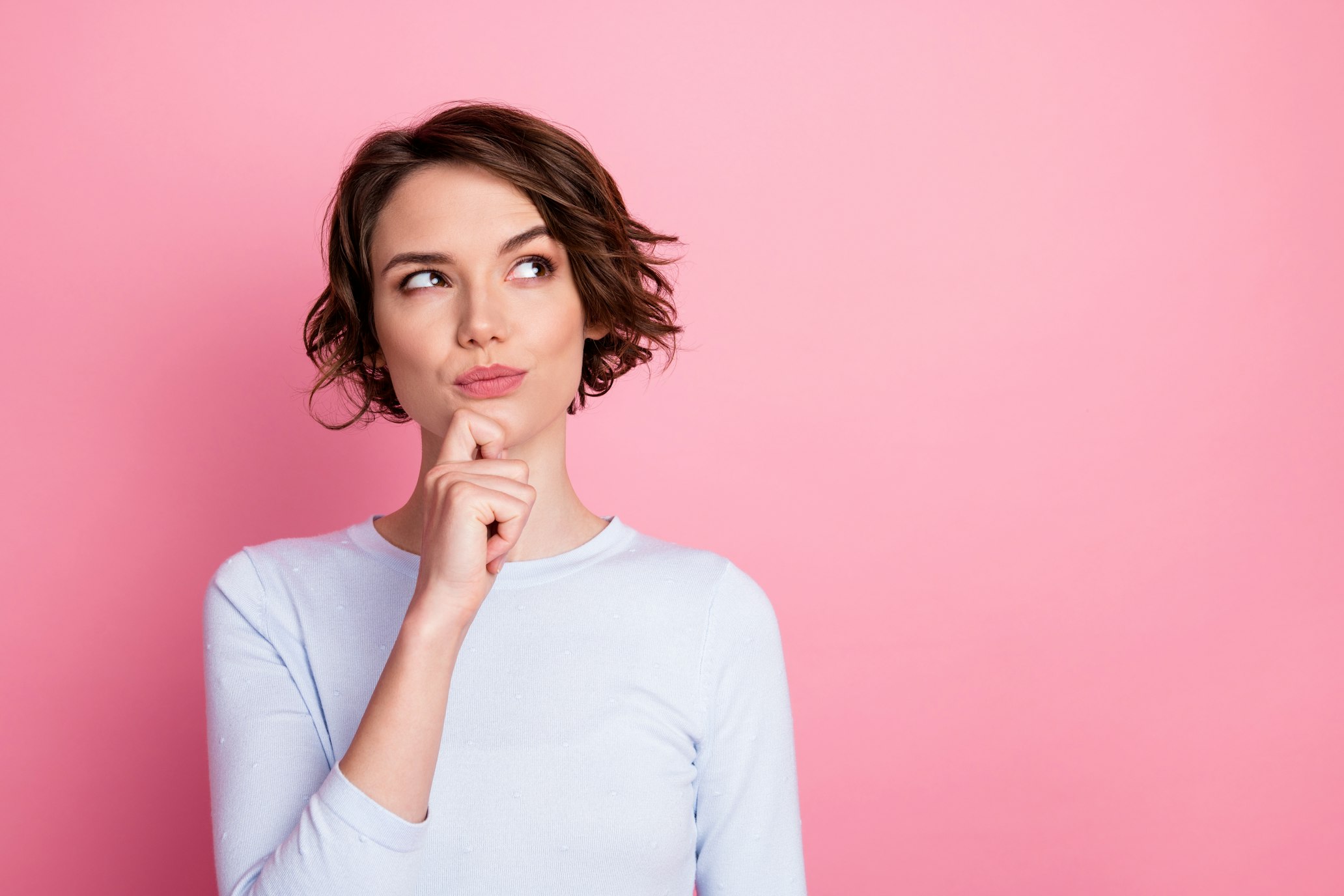 Focused girl looking to the side, touching her hand to the chin, making a decicion, wearing pullover isolated pastel color background