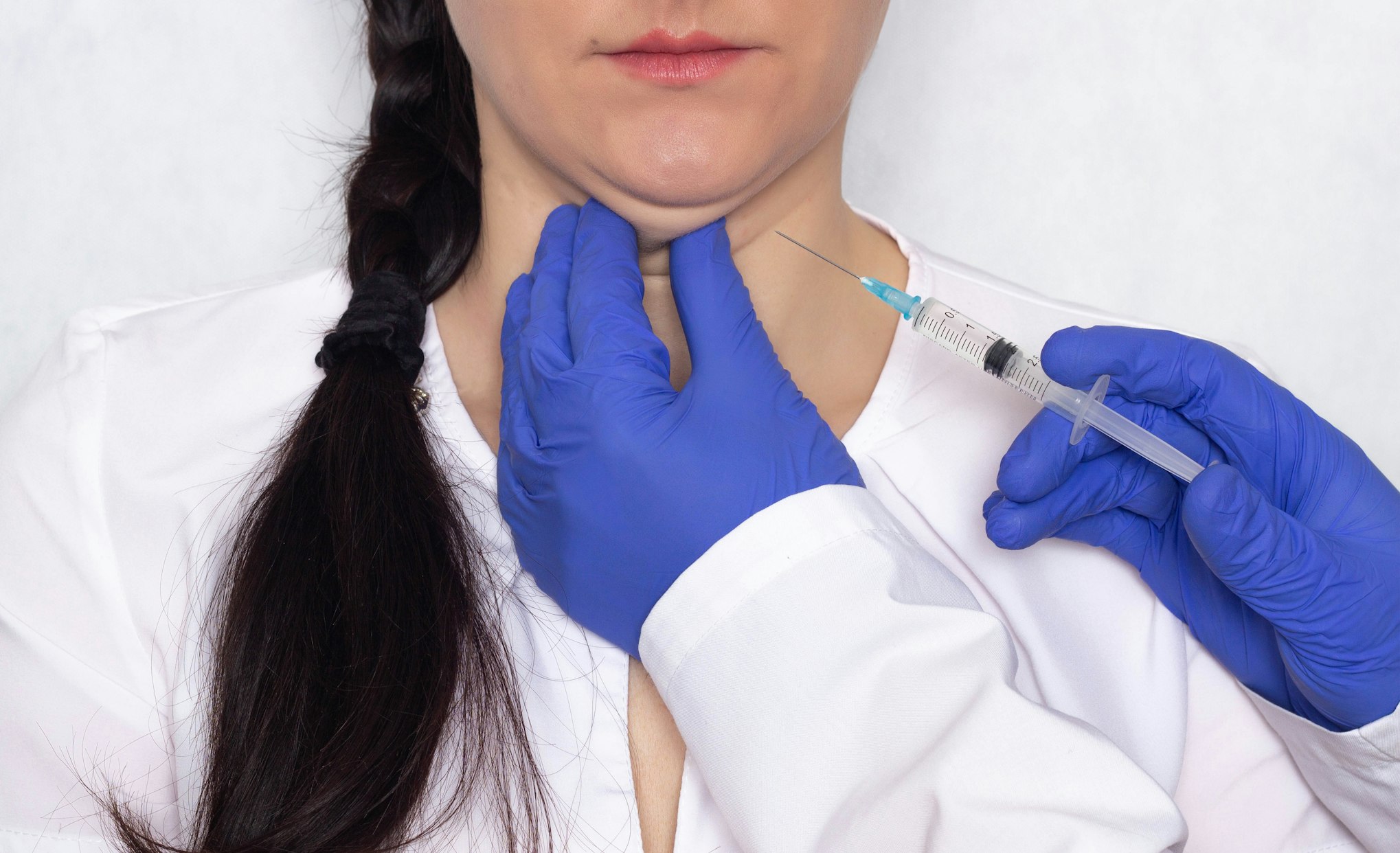 Doctor gives lipolytic injection to a caucasian girl's double chin on a white background, medical, close-up