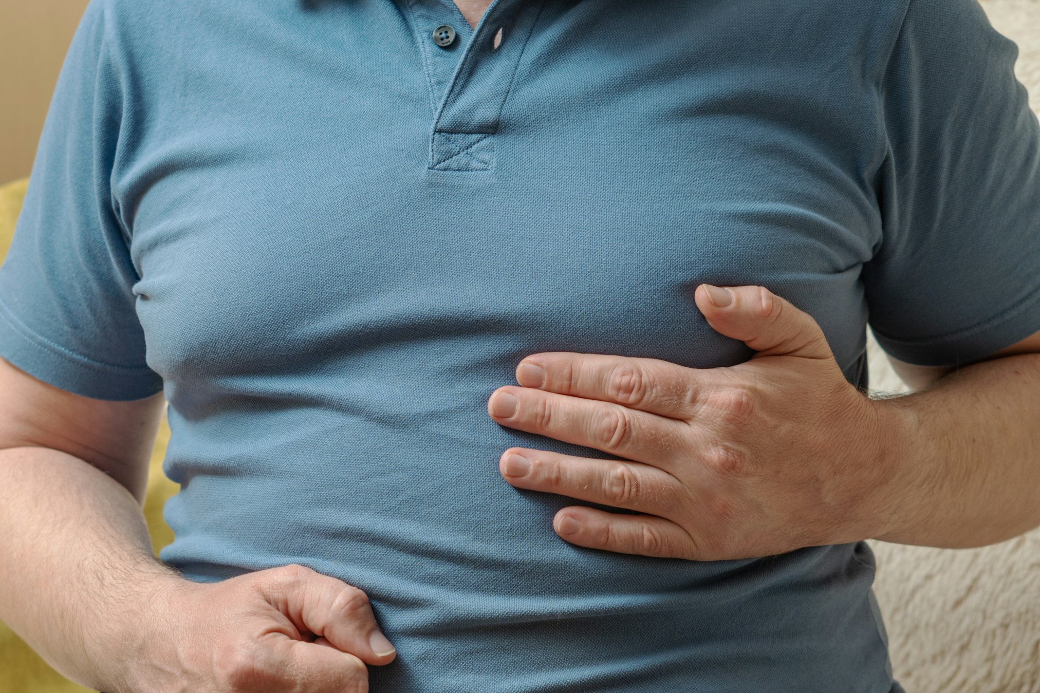 A man in a blue T-shirt holds his hands in his chest