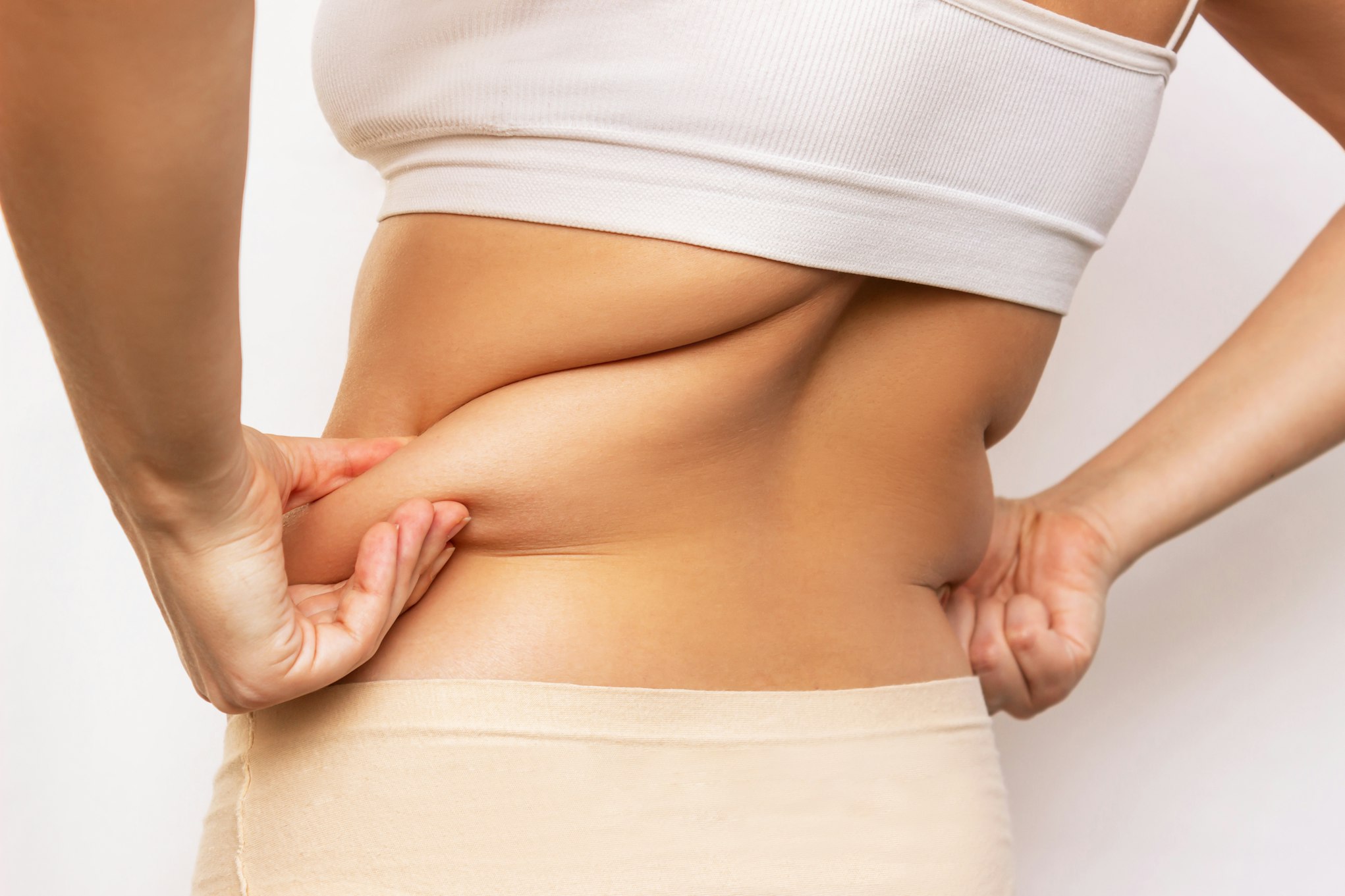 Cropped shot of a young woman holding fat folds on her back isolated on a white background