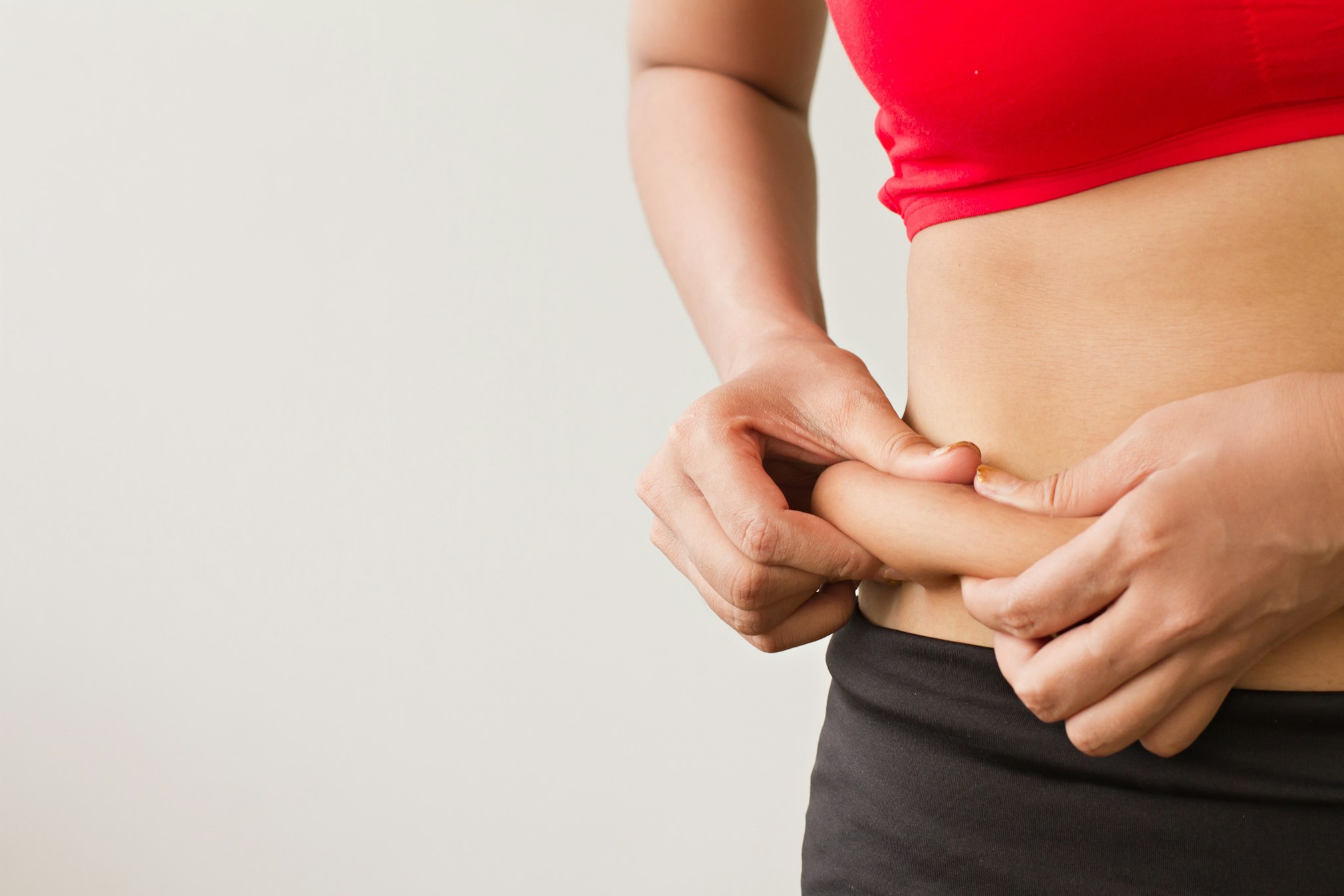 Woman's hand pinching her excess belly fat
