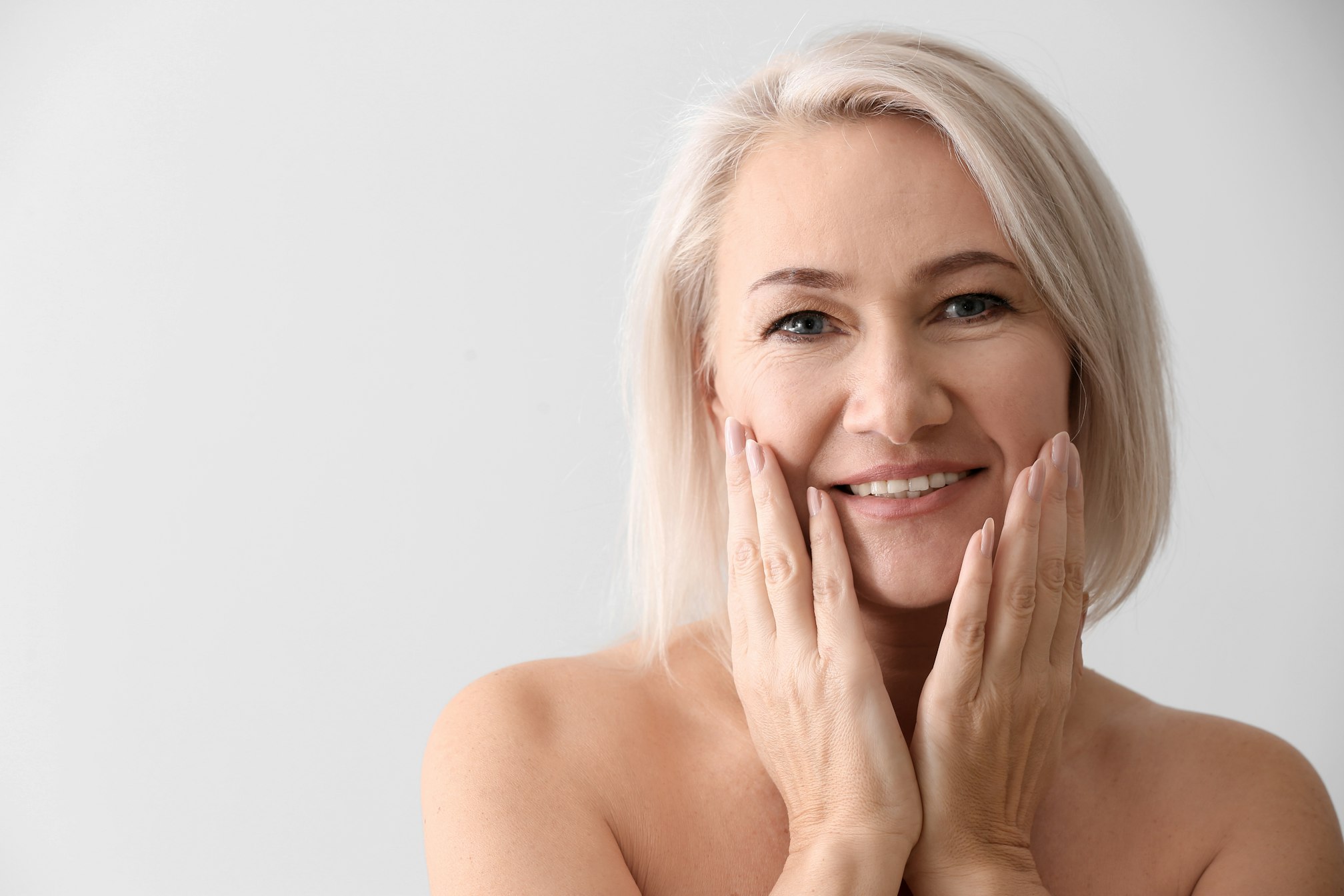Mature woman giving herself face massage on light background