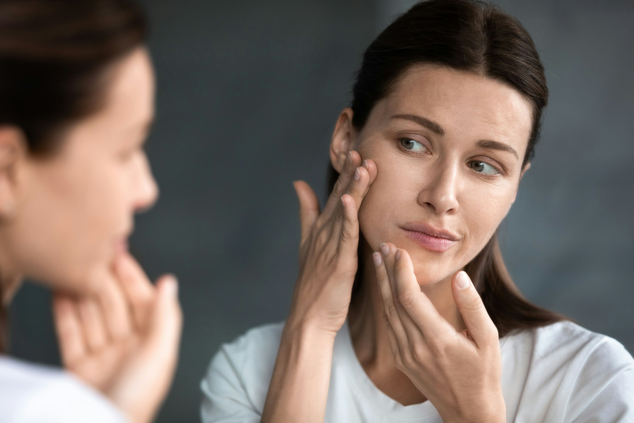 Woman touching face and looking in mirror