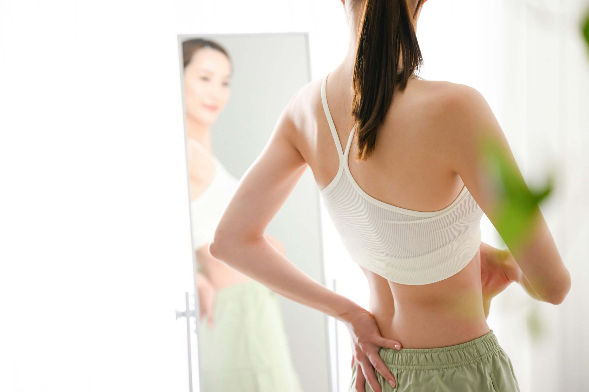 woman looking in the mirror with a hand on her lower back