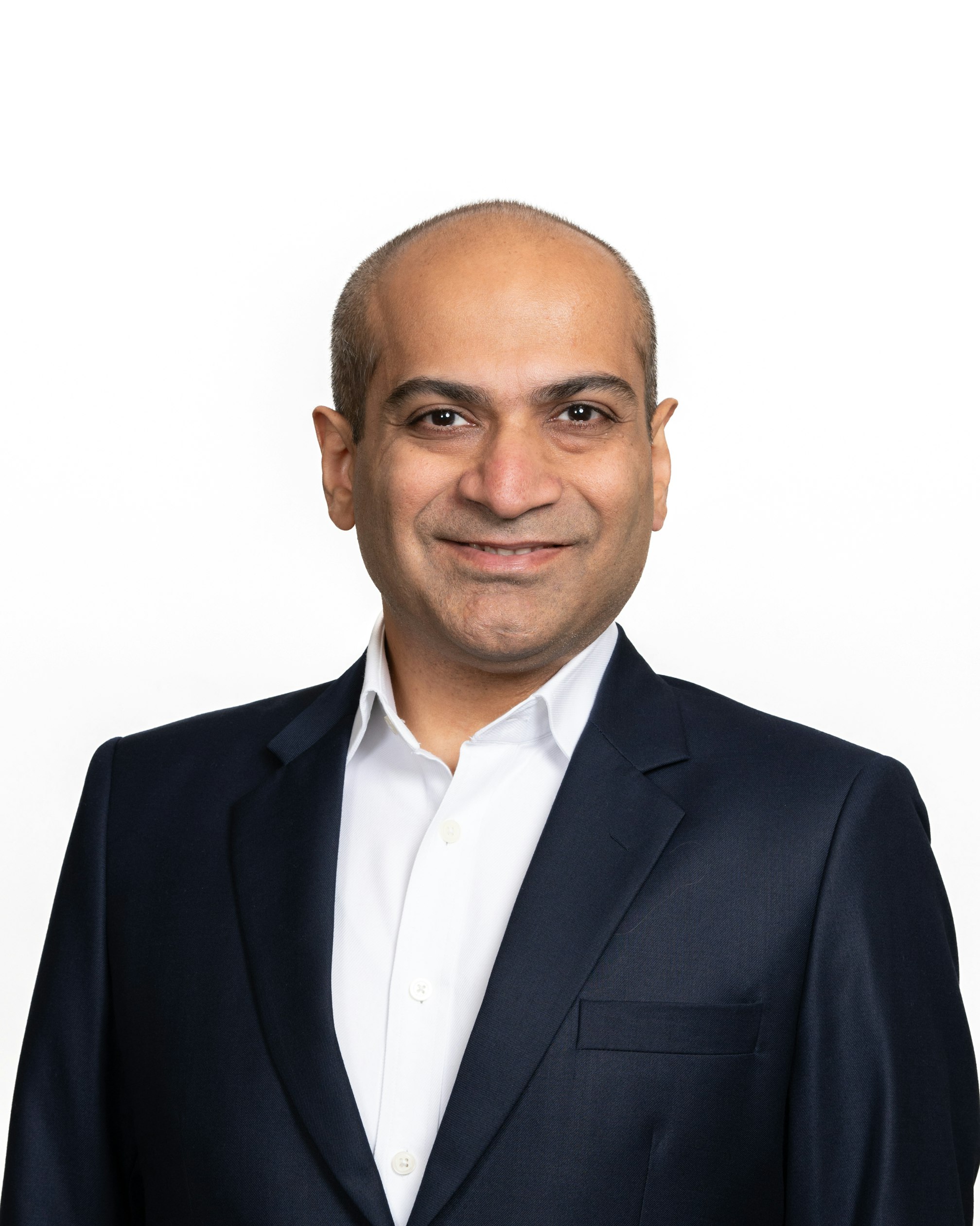 Headshot of AirSculpt CEO Yogi Jashnani posing with his arms crossed and smiling, wearing a dark jacket and blue shirt