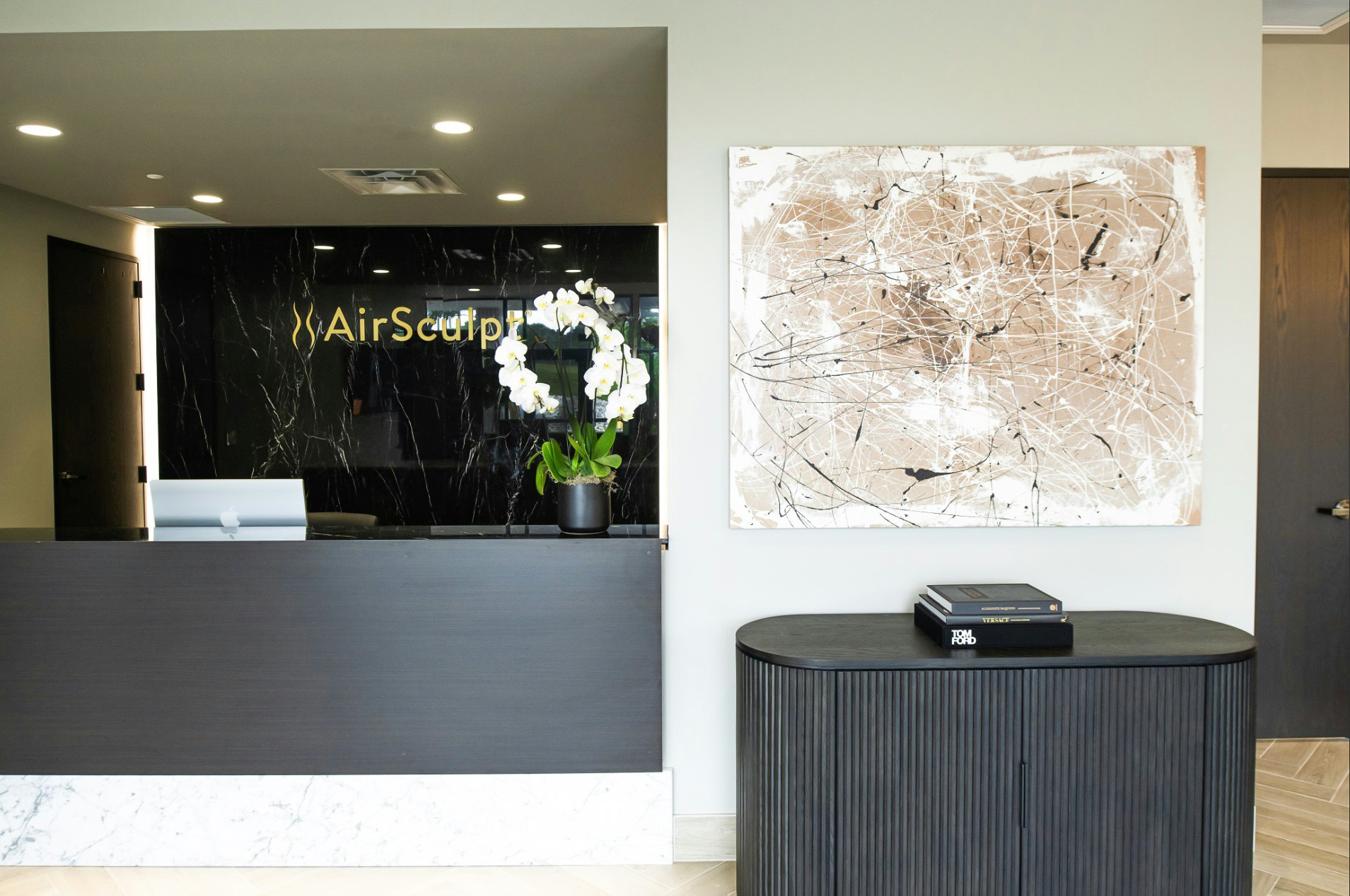Front desk with illuminated AirSculpt logo and abstract wall art in AirSculpt Body Contouring Kansas City clinic lobby