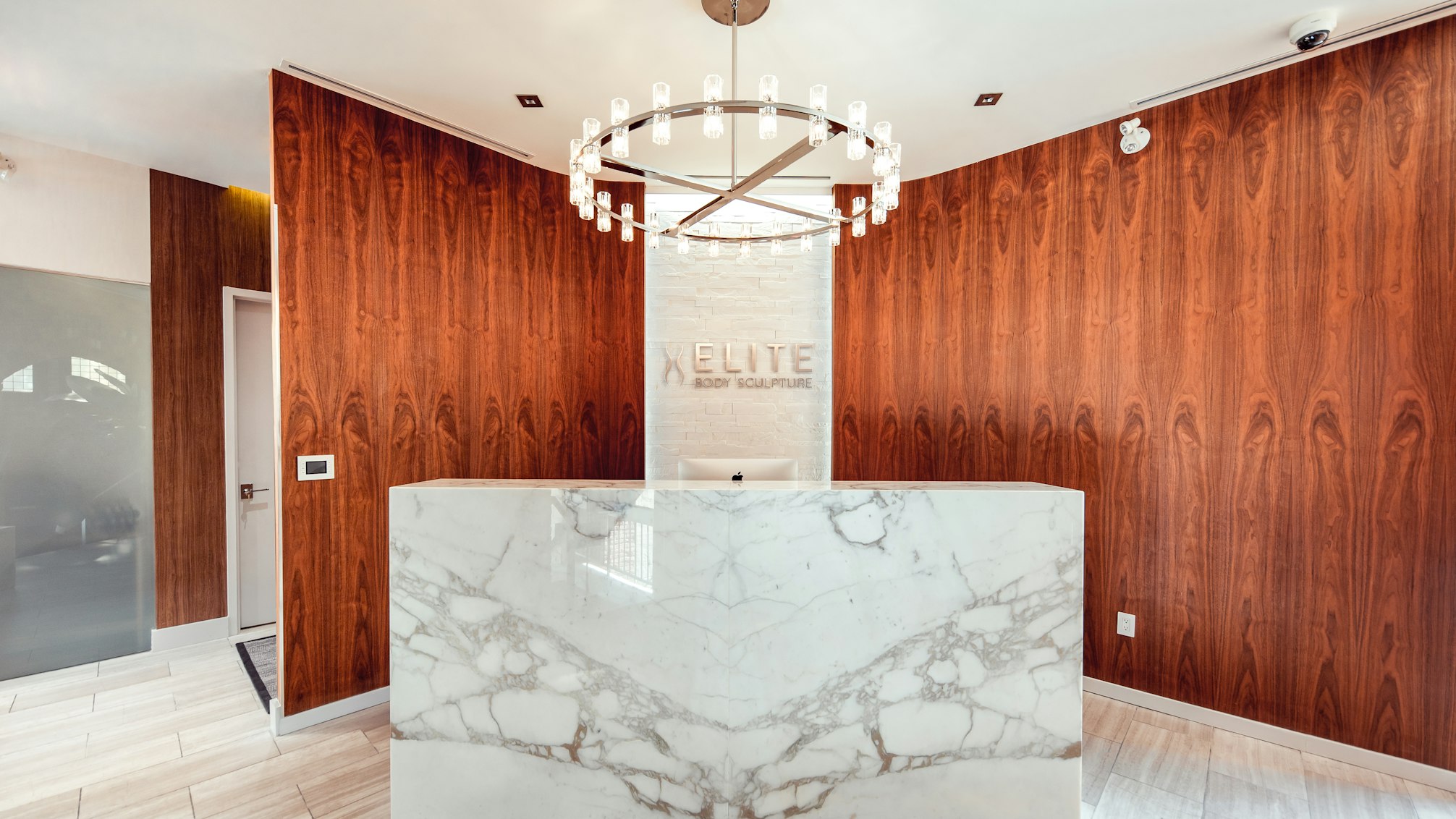Front desk with marble countertop and wood-paneled backdrop featuring Elite Body Sculpture logo in Elite Body Sculpture Toronto clinic lobby