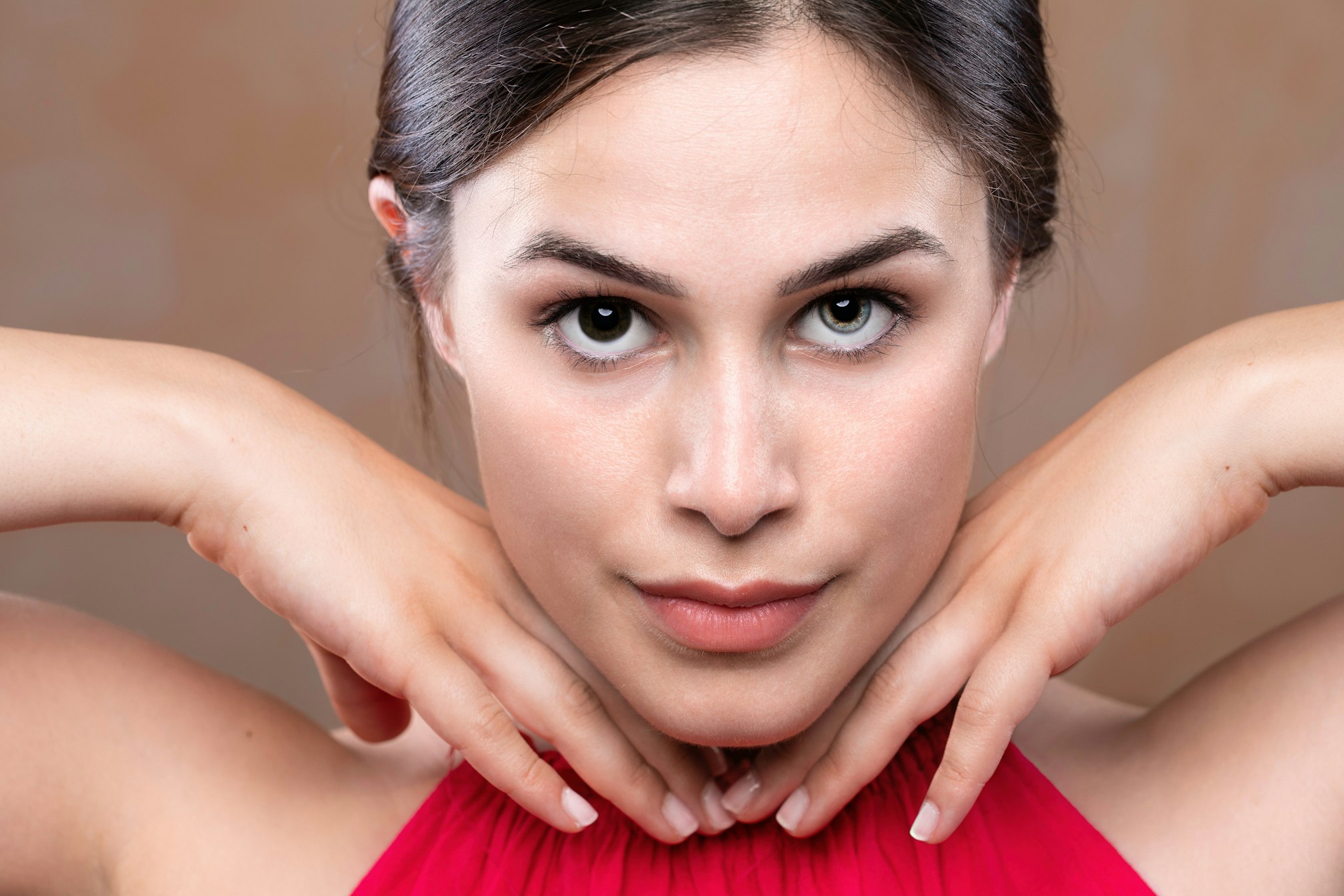 A stunning brunette girl shows confidence in appearance as she poses with hands under chin,