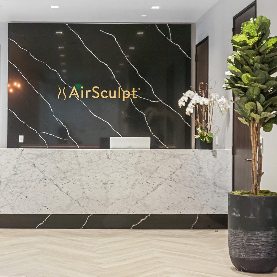 Front desk with black marble backdrop and illuminated logo in AirSculpt Body Body Contouring Clinic lobby