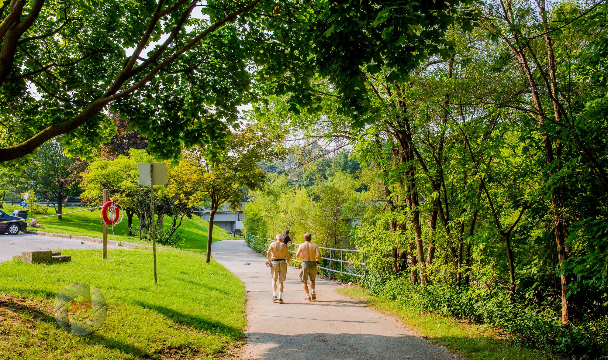 Two shirtless men jogging on a trail in a park