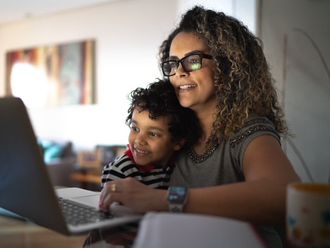 Mature woman working at home, carrying young son