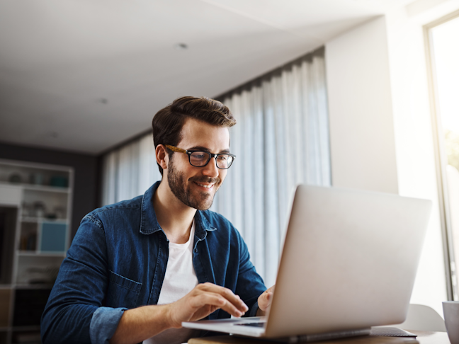 A handsome young businessman sitting down and using his laptop while working from home