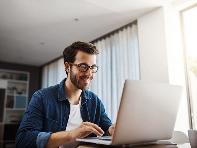 A handsome young businessman sitting down and using his laptop while working from home