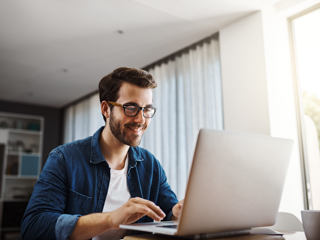 A handsome young businessman sitting down and using his laptop while working from home