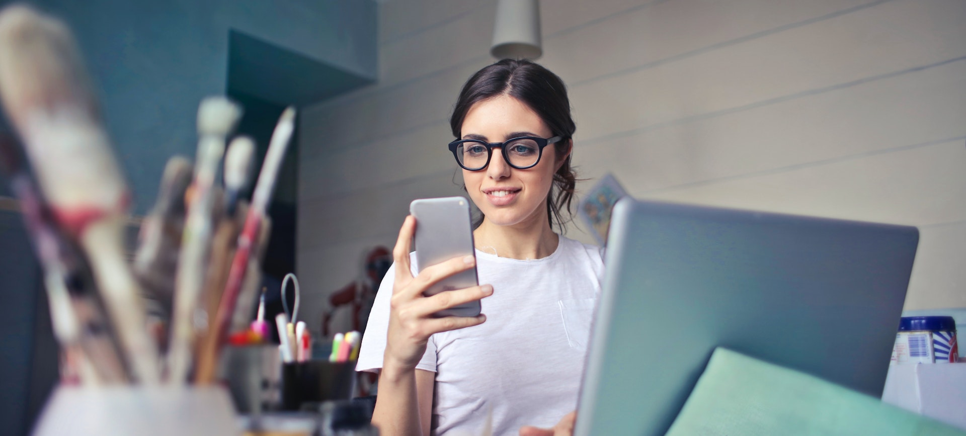 A young woman at her computer with phone in hand