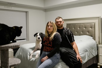 A woman and a man sitting on a bed with a dog