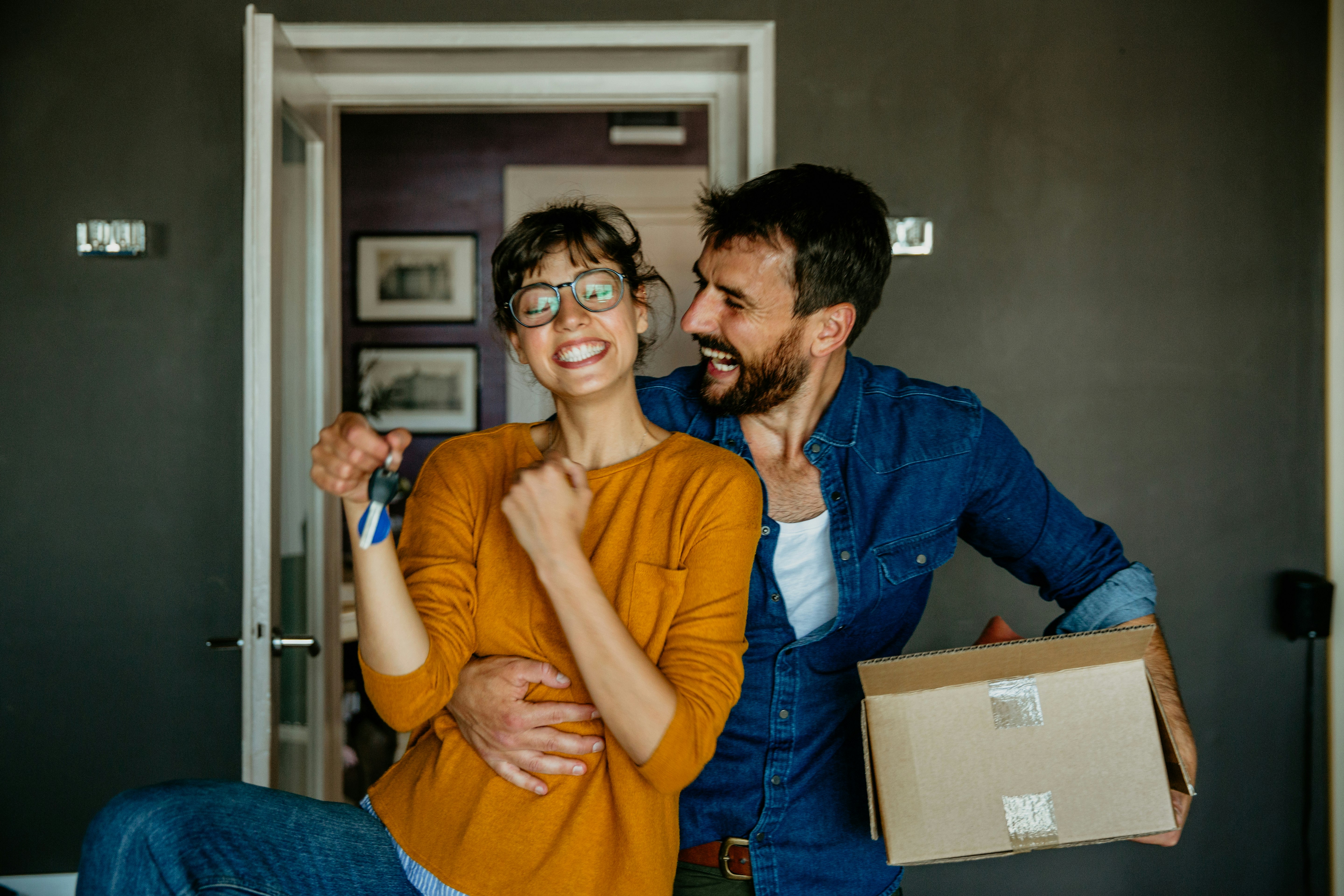 An excited man and woman holding keys and a cardboard box