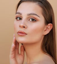 A woman with brown hair touching side of her face