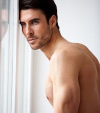 Shirtless man looking out the window