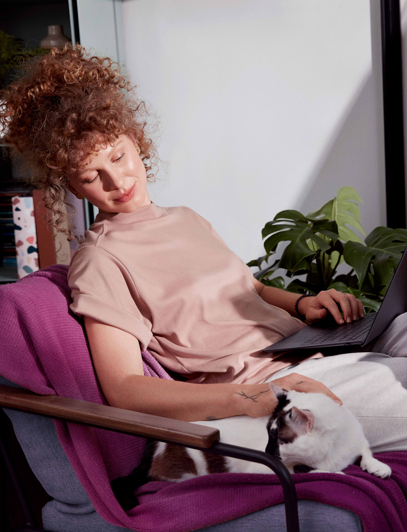Imagem de uma mulher usando um notebook sentada em um sofá com um gato ao lado