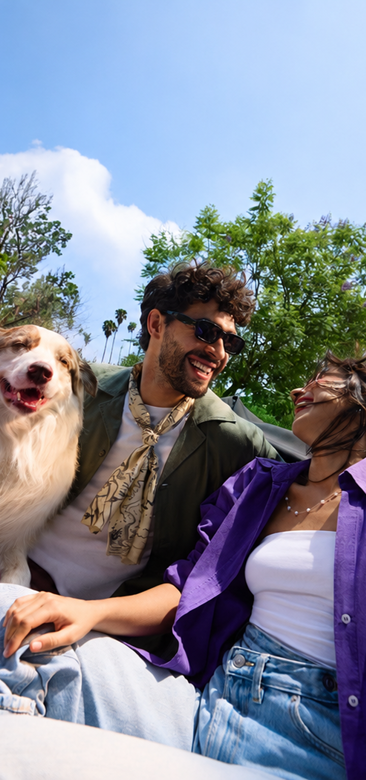 Pareja ríe al aire libre con su perro bajo un cielo azul despejado