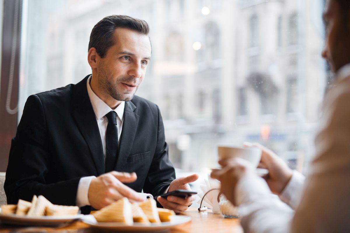 Portrait of two businessmen having discussion in warm lit cafe: brunette middle-aged gentleman talking to a man out of frame gesturing actively and smiling|fictitious 3d rendering of a modern living room with my own drawing|Young Military Couple Looking Inside Custom Kitchen and Design Drawing Combination.