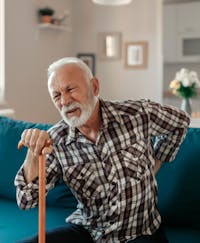man with cane wincing in pain and touching lower back