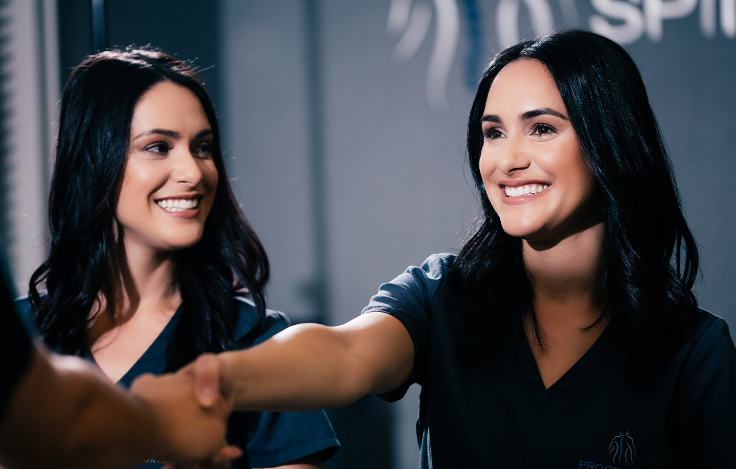 two women in dark scrubs smiling