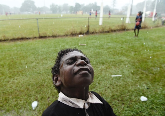 A young football fan feels the rain on his face minutes before kick-off for the Tiwi Islands grand final – the muddiest game of football.