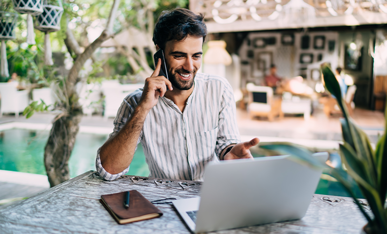 An employee working remotely, sitting near a beach or a pool.